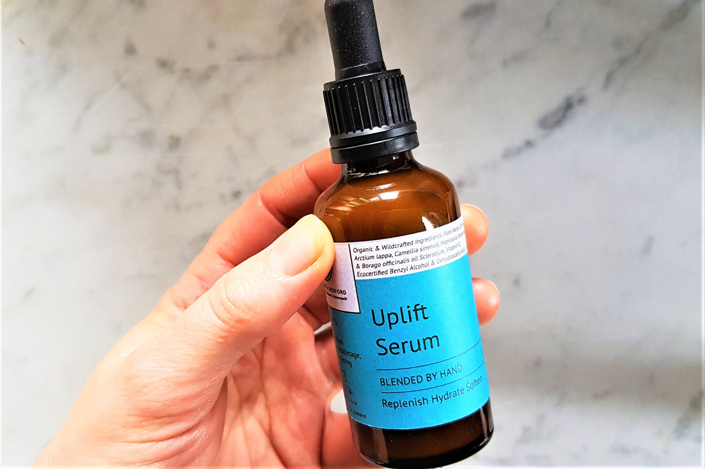 blue labelled amber dropper bottle held in pale hand against grey background